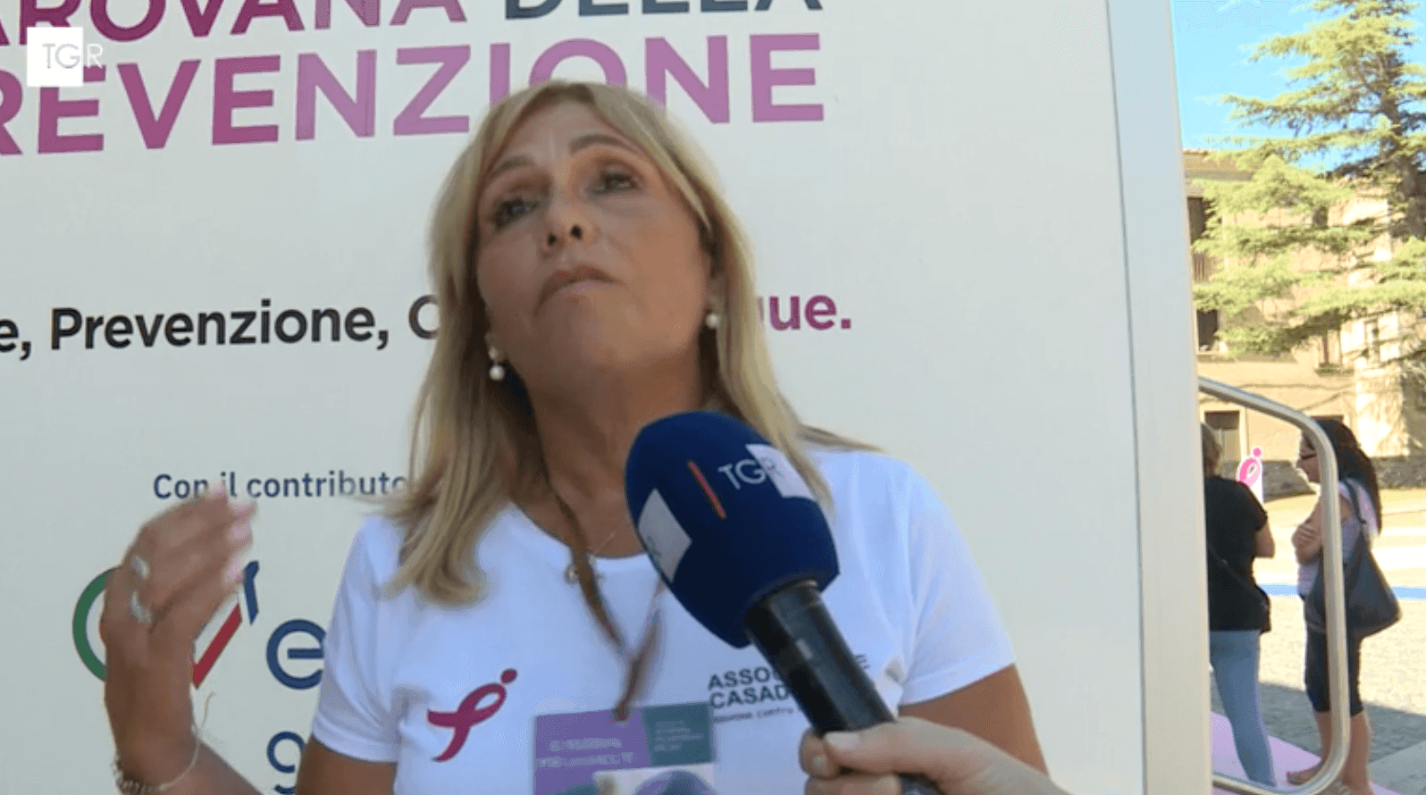 Woman speaking to a TGR microphone, background sign about prevention and outdoor setting with trees.