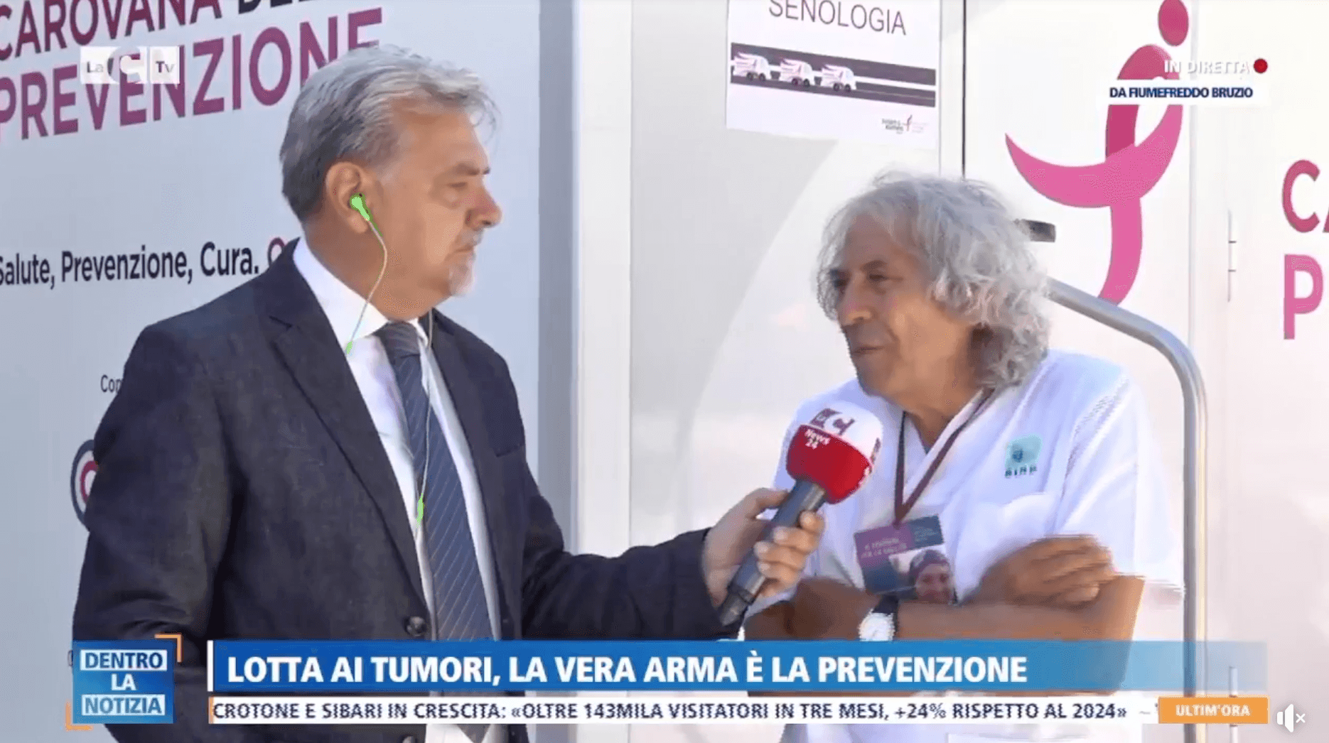 Two men discussing in front of a cancer prevention awareness banner, one holding a microphone.
