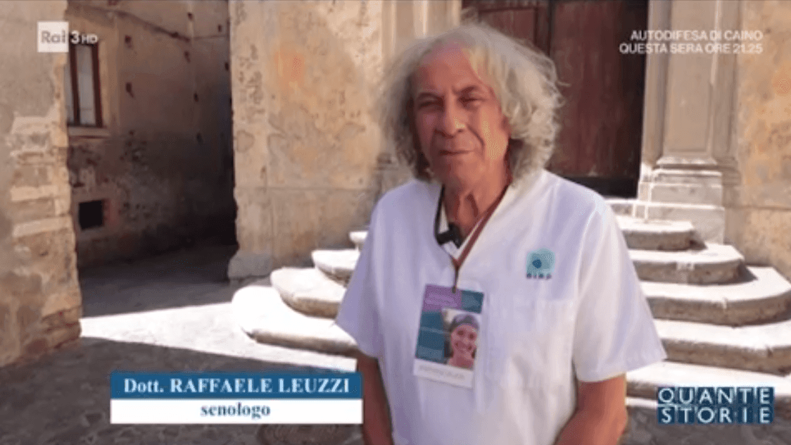 Person standing outside a historic building with stone steps, wearing a white shirt and an ID badge.